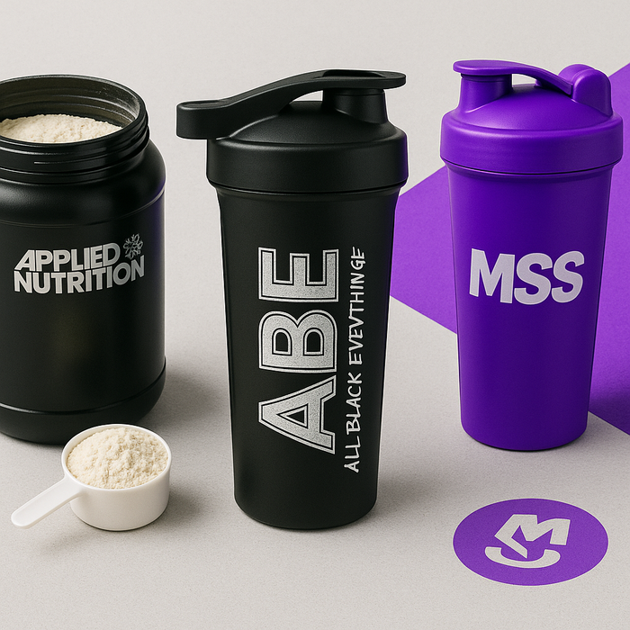 ABE shaker standing upright on a countertop, next to an open tub of protein (either Applied Nutrition or MSS-branded), with a scoop of powder ready to go. To one side, a bold MSS-purple shaker brings in that unmistakable pop of colour.