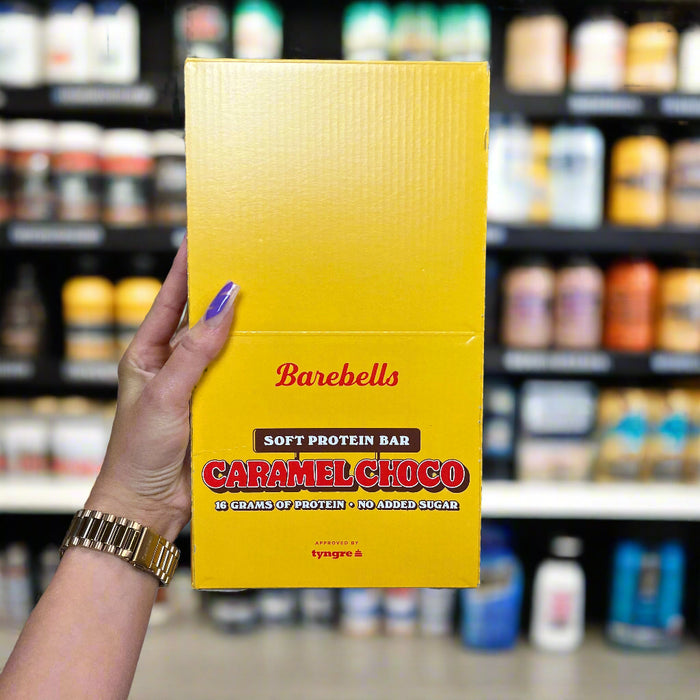 Close-up of (Barebells Soft Protein Bar 12x55g) held up inside My Supplement Shop, clearly showing the front label in a Sports Nutrition setting.