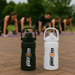 Black and white Per4m water bottles on a brick surface with people doing outdoor HIIT training in the background
