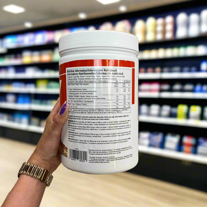 Close-up of PER4M Whey Protein Powder 900g) held up inside My Supplement Shop, clearly showing Nutritional Values on the packaging in a Sports Nutrition setting.